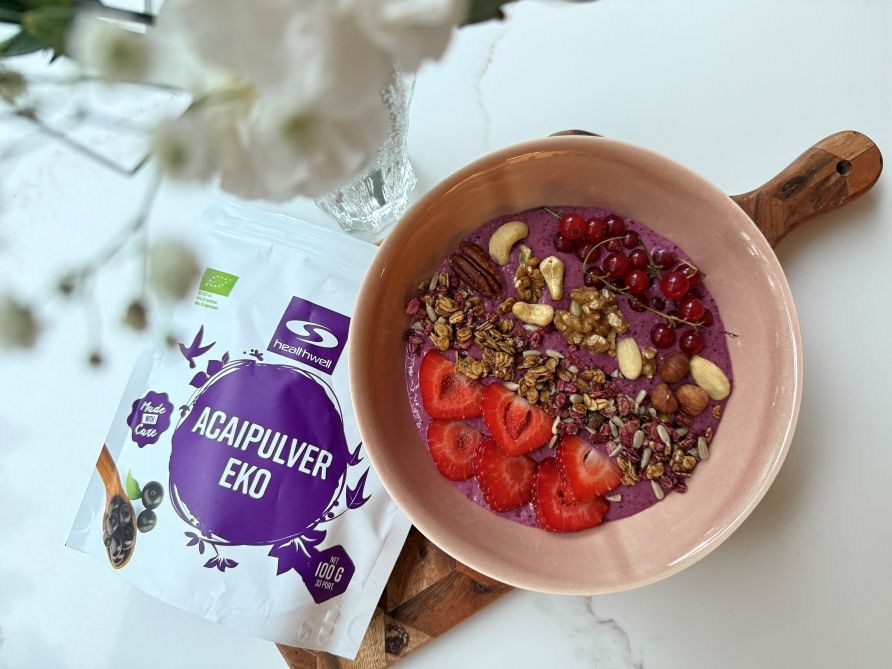 Lila Acai-smoothiebowl, jossa koristeena mansikkaa, granolaa, p�hkin�it� ja punaisia viinimarjoja.