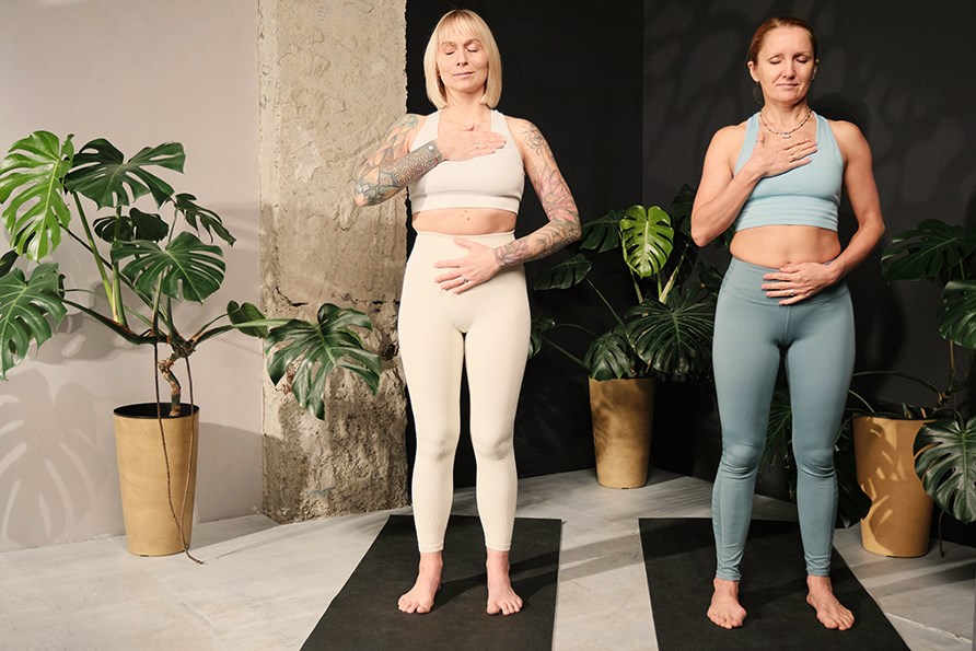 Kaksi rentoutunutta, tyytyv�ist� naista tekee hengitysharjoituksia joogastudiolla seisten joogamatoilla.