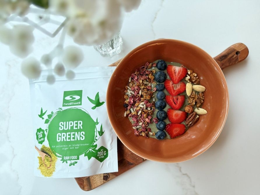 Green-smoothiebowl lautasella, koristeena mansikoita, mustikoita, p�hkin�it�, granolaa.