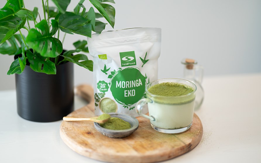 Puinen tarjotin, jolla on kupillinen moringalatetta ja pussi Healthwell Moringa EKO:ta.