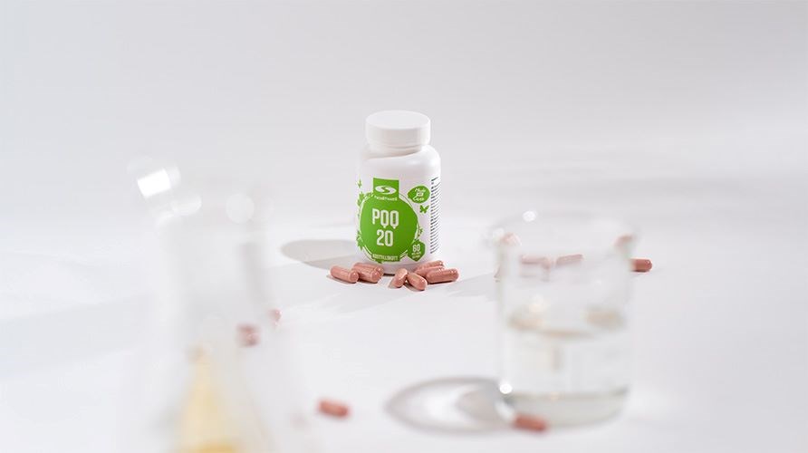 Purkillinen Healthwell PQQ:ta ja Healthwell PQQ:n kapseleita valkoisella pydll, valkoisella taustalla, sek mittalasilla.