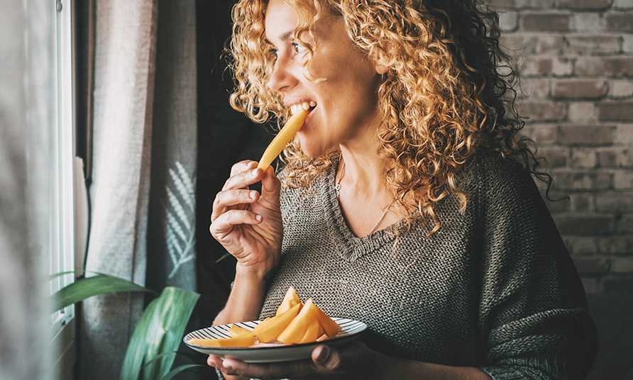Nainen seisoo ikkunan ��ress� ja sy� hedelm�lohkoja.