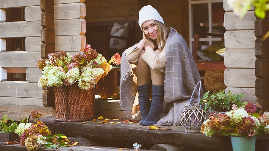 Nainen istuu talonsa ulkopuolella portailla syksyisessä ympäristössä. Nainen istuu talonsa ulkopuolella portailla syksyisessä ympäristössä.