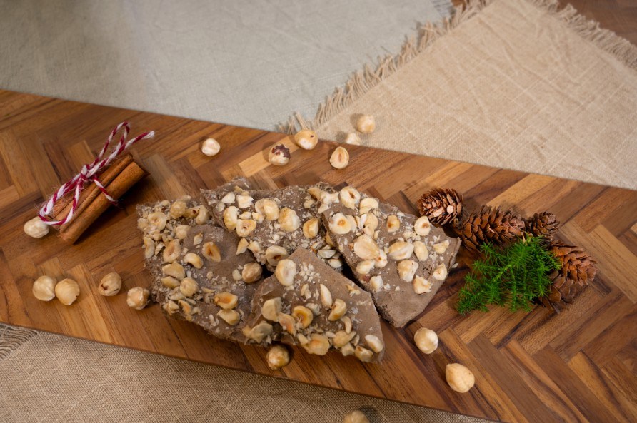 Jouluisen jogurttilevyn paloja leikkuulaudalla kanelitankojen, k�pyjen ja hasselp�hkin�iden kera.